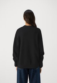 Svart oversized tröja med rund halsringning, ribbade ärmslut och en avslappnad passform, parat med lösa denimjeans. Slät textur utan mönster.