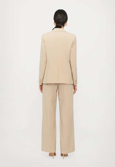 Beige getailleerde blazer en wijde broek, gladde stof, gestructureerd ontwerp, sluiting met één knop en subtiele hardwaredetails.