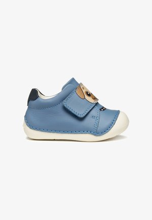 Chaussure en cuir bleu avec une sangle à crochets et boucle arborant un design de visage de chien. Bout en caoutchouc blanc et détails de couture contrastés.