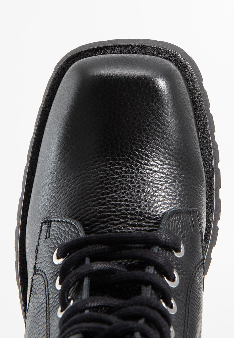 Bottes en cuir noir avec une finition texturée, dotées d'un bout arrondi, de lacets noirs et d'œillets en argent, montées sur une semelle en caoutchouc noir robuste.