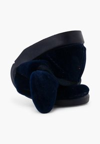 Navy fluwelen slide sandaal met een gebogen ontwerp, rubberen zool en een opvallende strikaccent. De textuur is zacht en pluisachtig, met gladde randen.