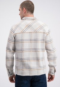 Witte geruite blouse met grijze, zwarte en gele accenten, gestructureerde stof, geknoopte manchetten en een kraag, gezien van achteren.