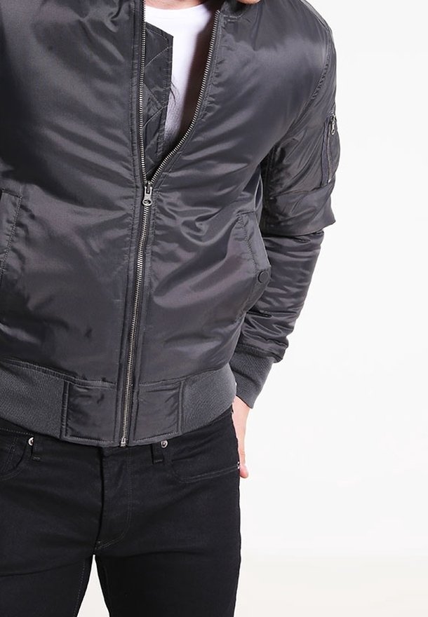 Veste bomber grise en nylon lisse avec fermeture éclair, poignets et taille côtelés. Comprend une poche latérale sur la manche.