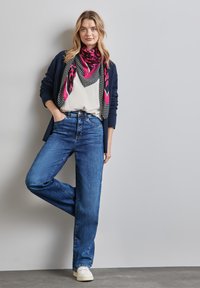Jeans a gamba larga blu scuro indossati con una maglietta bianca, una sciarpa decorata in rosa e nero e un cardigan blu navy scuro. Sneakers bianche.