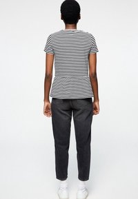 Svart och vit randig kortärmad topp med peplummidja, kombinerad med högmidjade mörka jeans och vita sneakers.