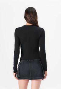 Black long-sleeve shirt paired with a dark denim mini skirt featuring side pockets and a raw hem. Simple, fitted design.
