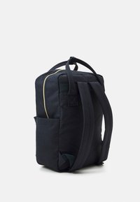 Rygga i mörkblått tyg med gulddragkedja, vadderade remmar och en sidoficka; rektangulär form med quiltad textur på sidorna.