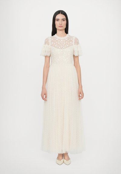 Das Kleid hat einen durchsichtigen, bestickten Oberteil mit kurzen, voluminösen Ärmeln und ist kombiniert mit einem fließenden, gefalteten Rock aus weichem Cremestoff.