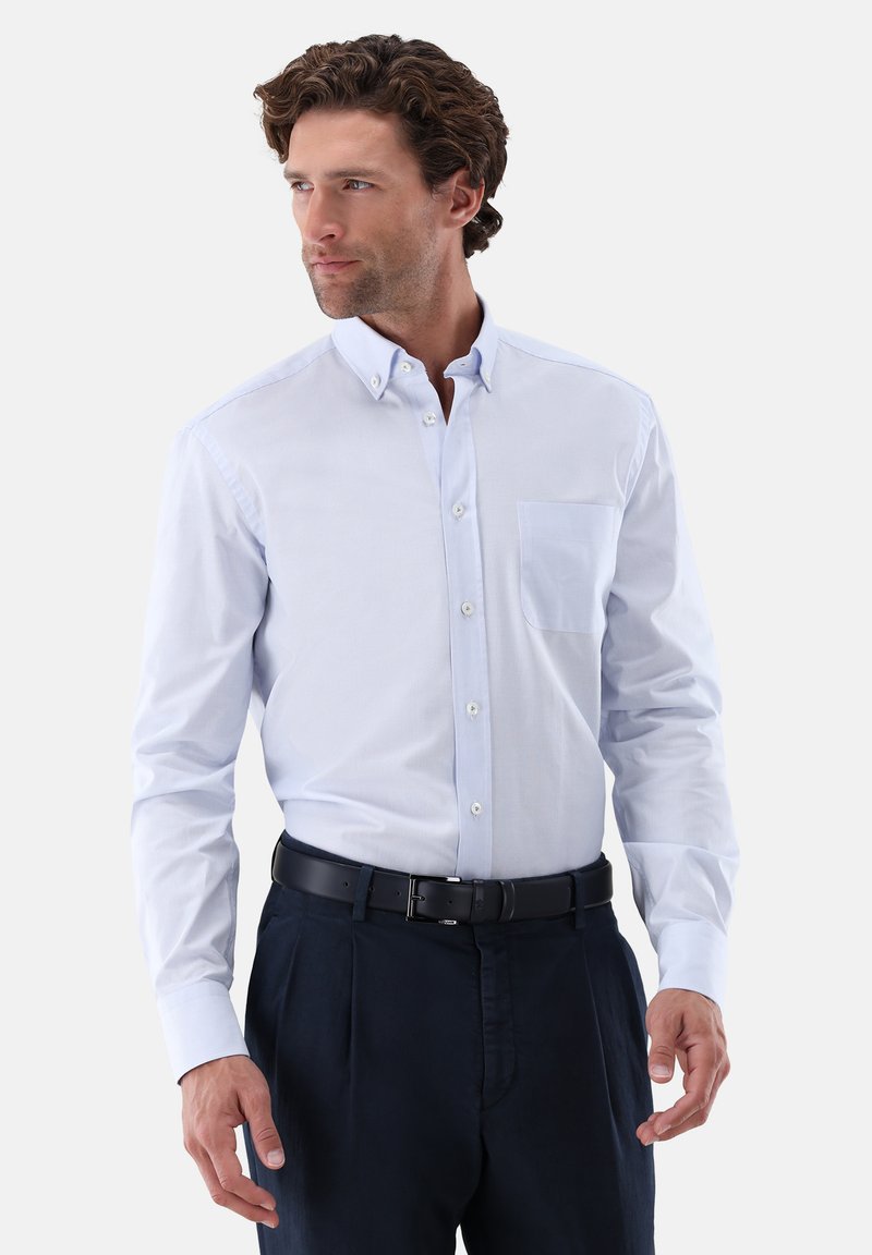 Hellblaues Hemd zum Knöpfen mit einer Brusttasche, langen Ärmeln und Kragen; kombiniert mit dunklen Hosen und einem schwarzen Gürtel.