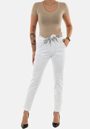 T-shirt beige ajusté avec un décolleté en bateau, associé à un pantalon blanc taille haute avec une ceinture en tissu noir et blanc à motif.