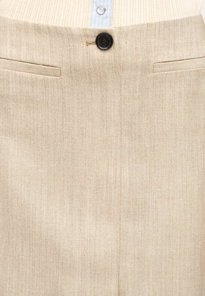 Μπεζ λινά παντελόνια με ένα μαύρο κουμπί και δύο οριζόντιες τσέπες με σχισμές, συνδυασμένα με μπλε και λευκό ριγέ πουκάμισο.