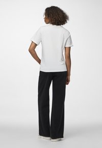 Biała bawełniana koszulka z krótkimi rękawami i okrągłym dekoltem, w połączeniu z czarnymi, szerokimi spodniami z wysokim stanem i białymi trampkami.