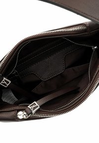 Brūnas ādas somas iekšpuse ar rāvējslēdzēja nodalījumu, gludu tekstūru un mazu logotipa plāksteri. Redzami sudraba aparatūras elementi.