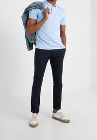 Svetle modré polo tričko s malým logem, v kombinaci s námořnickými kalhotami, bílými teniskami a denimovou bundou přehozenou přes rameno.