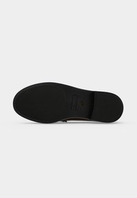 Semelle d'une chaussure habillée noire avec des zones de grip texturées au talon et à l’orteil, affichant les indications de taille et de marque près de la voûte plantaire.