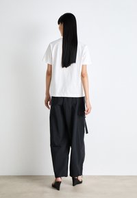 T-shirt en coton blanc à manches courtes associé à un pantalon cargo noir ample avec des accents zippés et un design de jambe fuselée.