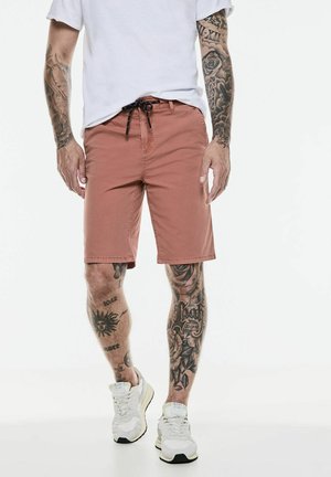 Roze shorts met een verstelbaar trekkoord, een vlakke voorkant en omgezoomde randen, gecombineerd met witte sportschoenen.