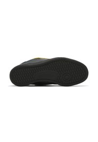 Black athletic shoe sole with textured pattern and circular logo detail. Features yellow accents and a smooth, durable material finish.