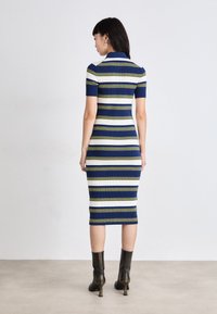 Jūras spēku un baltu svītrotu ribotu kleitu ar īsām piedurknēm, pieguļošu siluetu un līdz ceļiem garu apakšmalu. Valkāta ar melniem papēžu zābakiem.