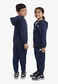 Sweat à capuche bleu marine et joggings, confectionnés en tissu doux. Comprend des poches avant, des poignets côtelés et des accents du logo Nike sur les deux pièces.