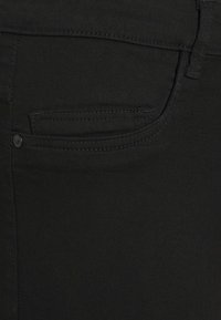 Tissu denim noir en gros plan montrant la poche avant avec des coutures détaillées et un petit rivet près du bord de la poche.