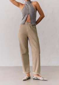 Top en denim gris à col halter avec fermeture éclair à l'avant, pantalon beige taille haute, et chaussures plates à motif serpent. Revers sur le bas du pantalon.
