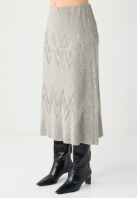 Grau gerippter Strickrock mit ausgestelltem Design und Zickzack-Ausschnitten. Kombiniert mit schwarzen Stiefeln mit spitzer Spitze und Absatz.