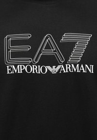 Zwart katoenen T-shirt met opvallende witte tekst: "EA7 EMPORIO ARMANI." De tekst combineert vaste en gestreepte letters, waardoor de merkidentiteit wordt benadrukt.