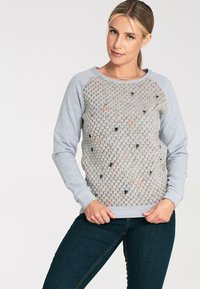 Jasnoszara bluza z teksturowanym, puchowym przodem z kolorowymi plamkami. Długie rękawy, okrągły dekolt oraz ściągacze na rękawach i dole.