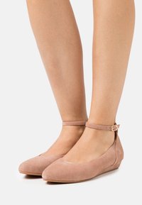 Rosa mockaskinn ballerinat med spetsig tå, vristrem och liten kilklack. Mjuk textur och minimalistisk design med ett säkert spänne.