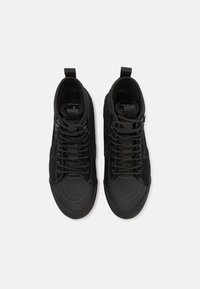 Sorte høyhælte sneakers med en glatt lær tåhette, strukturerte stoffpaneler, forsterkede snørehull og flate snøringer. To løftestropper bak på hælen.