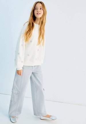 Hvid sweatshirt med sølvstjerne-mønstre, kombineret med lysegrå bukser med vide ben og cargo-lommer samt metalliske flade sko.