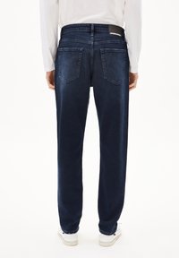 Donkerblauwe denim jeans met een recht model, met twee achterzakken en een zwart taillebandlabel, weergegeven vanuit de achterkant.