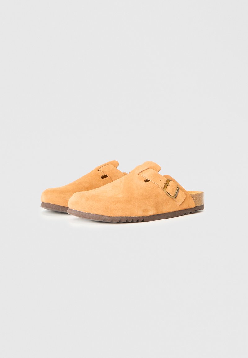 Ein Paar hellbraune Wildleder-Clogs mit verstellbarem Riemen und Messingschnalle, ausgestattet mit einem Korkfußbett und einer gerippten Gummisohle.