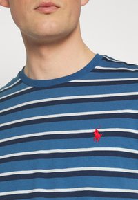 Kortärmad t-shirt med rund halsringning som har växelvis blå och vita ränder, med en röd broderad hästlogotyp på vänster bröstomr�åde.