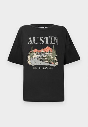 T-shirt preta de mangas curtas e corte largo, com um design gráfico de uma estrada, montanhas e cactos. O texto diz "AUSTIN TEXAS."