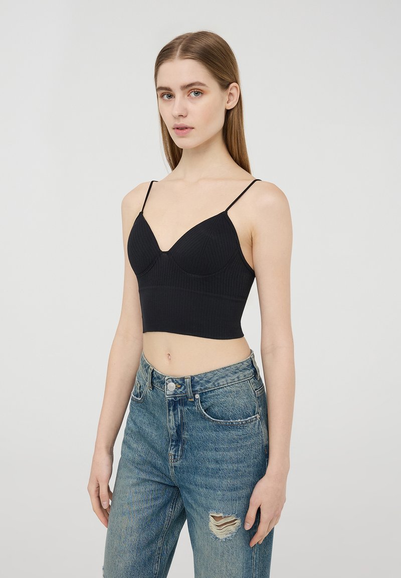 Top corto a coste nera con spalline sottili e regolabili, caratterizzato da un design del busto sagomato e una texture liscia, abbinato a jeans a vita alta strappati.