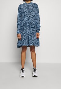 Blaues Blumenmusterkleid mit langen Ärmeln, einer gerafften Taille und einem ausgestellten Rock. Tragen Sie es mit weißen Turnschuhen für einen kontrastierenden Look.