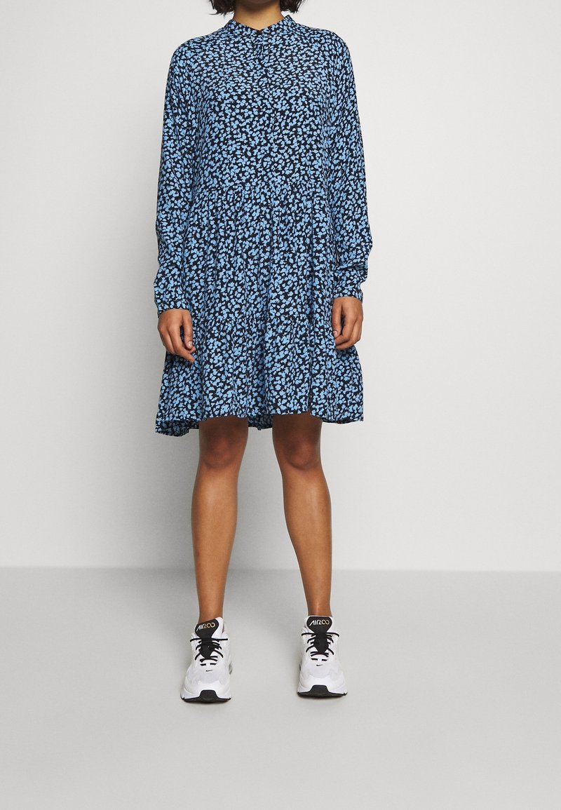 Blaues Blumenmusterkleid mit langen Ärmeln, einer gerafften Taille und einem ausgestellten Rock. Tragen Sie es mit weißen Turnschuhen für einen kontrastierenden Look.