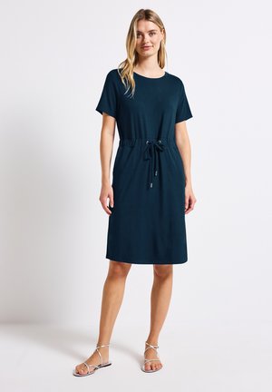 Mørk teal kjole med korte ærmer, elastisk snøre i taljen, glat stof, knælang og minimalistisk design. Flade sandaler fuldender looket.