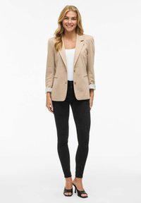 Beige blazer met twee knopen, opgerolde mouwen en klepzakken. Gecombineerd met zwarte skinny jeans en zwarte open teen hakken. Witte t-shirt eronder.
