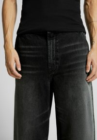 Svarta denimjeans med rak benform, kännetecknade av en urblekt textur och synliga sömdetaljer vid midjan.