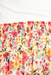 Saia floral com cintura franzida, apresentando flores multicoloridas em vermelho, amarelo e verde sobre um fundo claro; tecido texturizado com pregas.