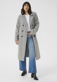 Cappotto doppiopetto grigio in misto lana con bottoni neri, caratterizzato da grandi revers e una vestibilità comoda, indossato sopra una maglietta bianca e jeans a gamba larga blu.