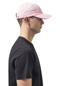 Roze baseballpet met een gebogen rand, gemaakt van katoen. Verstelbare band aan de achterkant, gedragen door een persoon in een zwart T-shirt, zijaanzicht.