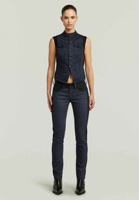 Gilet di jeans blu scuro, senza maniche, con bottoni frontali e tasche, abbinato a jeans slim-fit blu scuro con pannelli laterali neri.