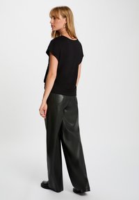 Top negro de manga corta con un corte relajado, combinado con pantalones de cuero verde de tiro alto y pierna ancha. Textura suave y diseño minimalista.