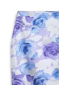 Gros plan sur le tissu d'une jupe avec des motifs de roses en aquarelle bleues et violettes et une petite poche horizontale sur un fond clair.
