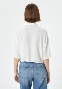 Blusa bianca a maniche corte con vestibilità ampia e tessuto strutturato, abbinata a jeans in denim blu a vita alta con tasche posteriori.