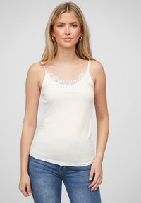 Hvit topp med tynne stropper, med en blond V-hals og en tettsittende design. Myk tekstur og glatt stoff.